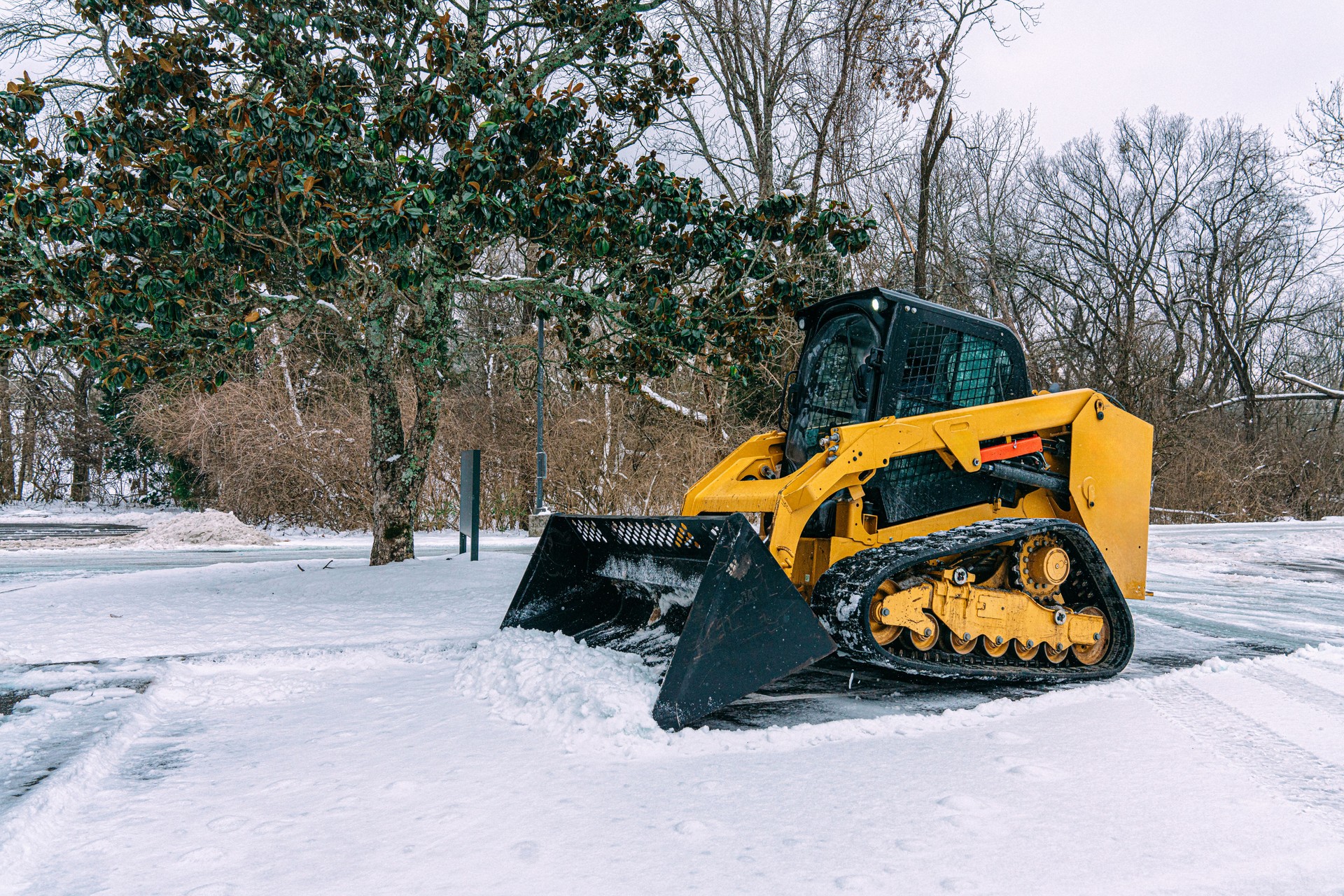 Snow Removal Company or a City Worker using the weight of a Bulldozer to scrape away snow and ice from a parking lot in Winter